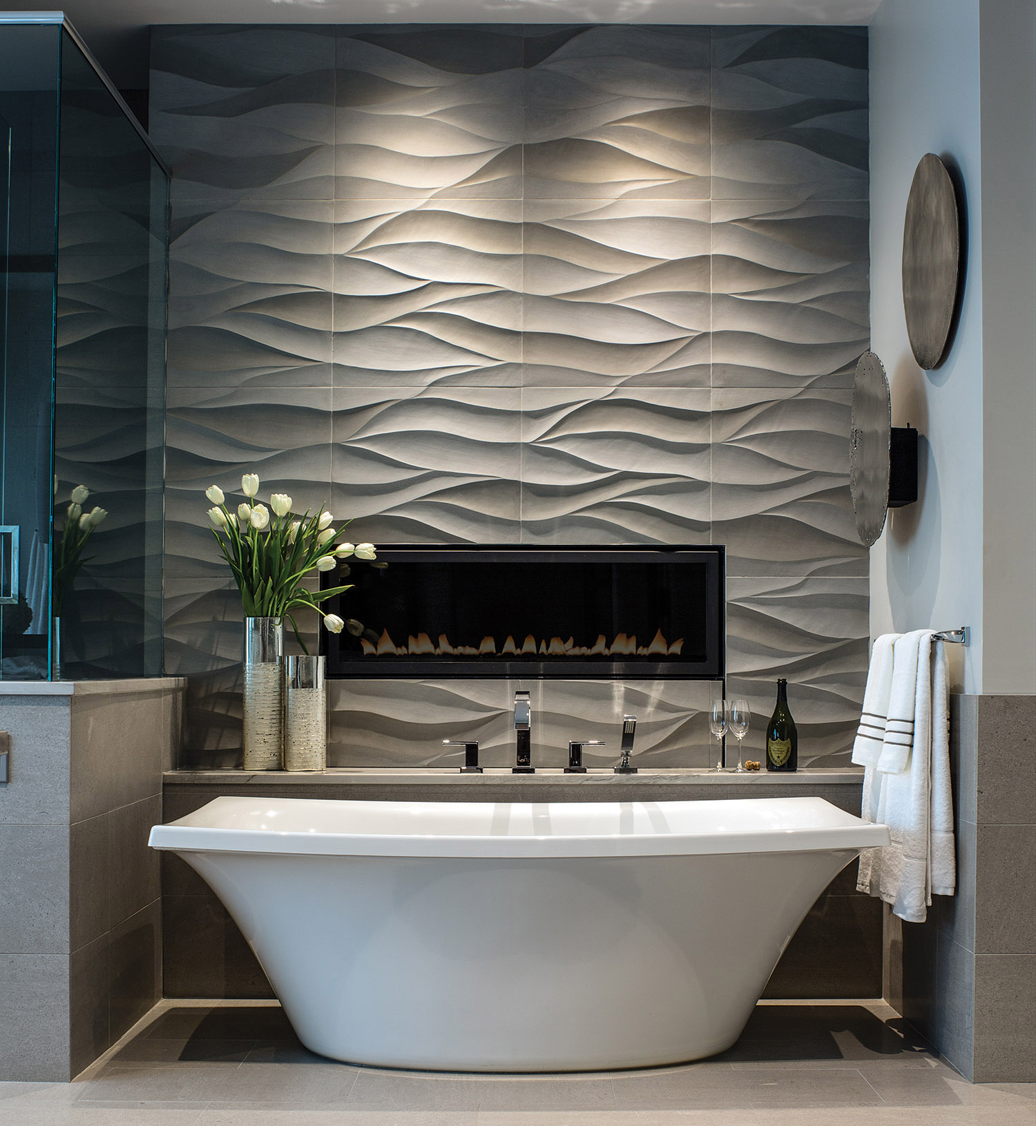 The contrast between the free-standing soaker tub and the wave-patterned tile wall adds drama to the master bath. The tile, carried in-house by Allard & Roberts, is carved stone. Lighting by Lux Lighting. At press-time, this photo had been added to almost 20,000 “ideabooks” on the website Houzz.com. Photo by David Dietrich